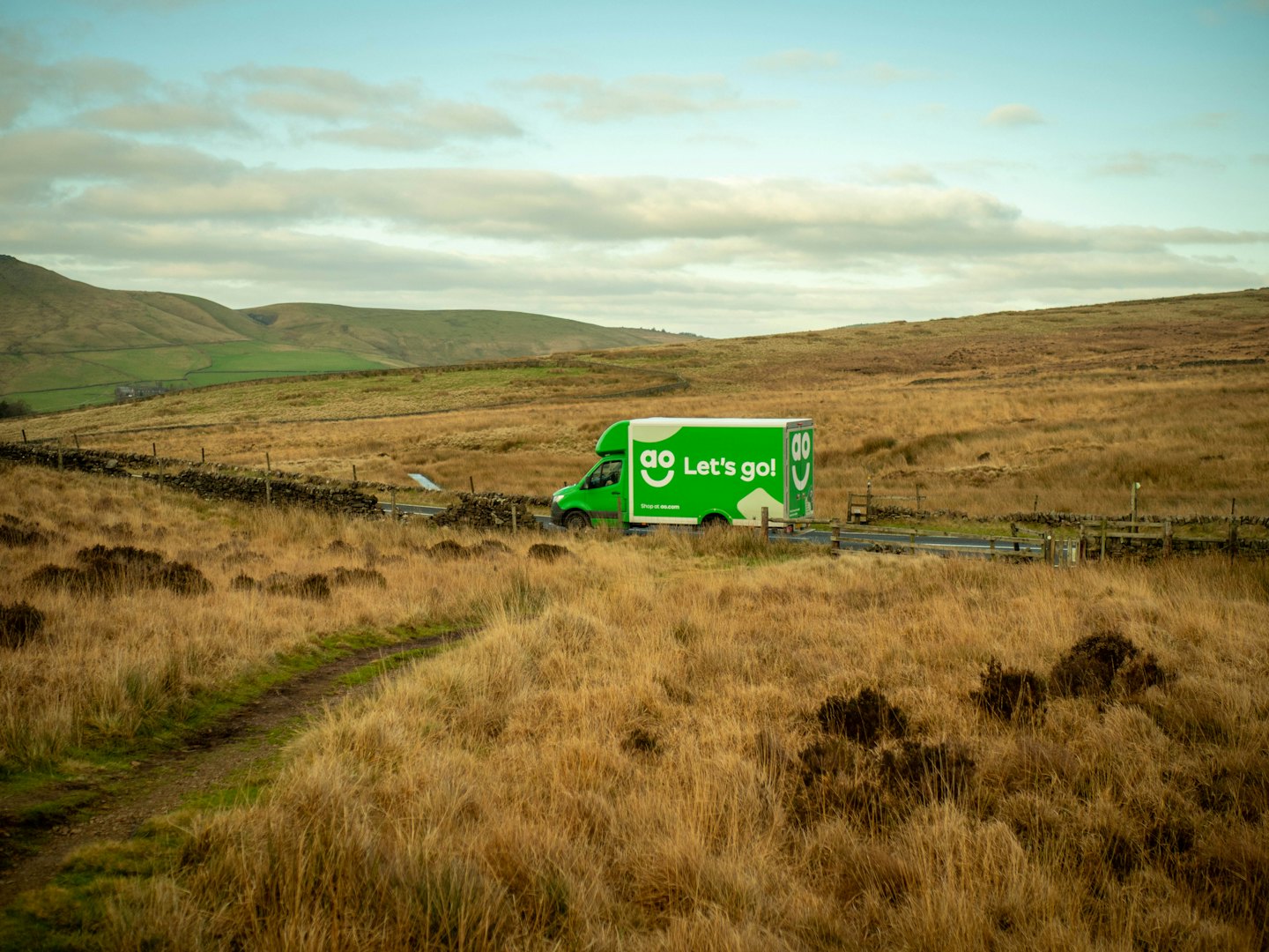 A green delivery van driving through a rural landscape.